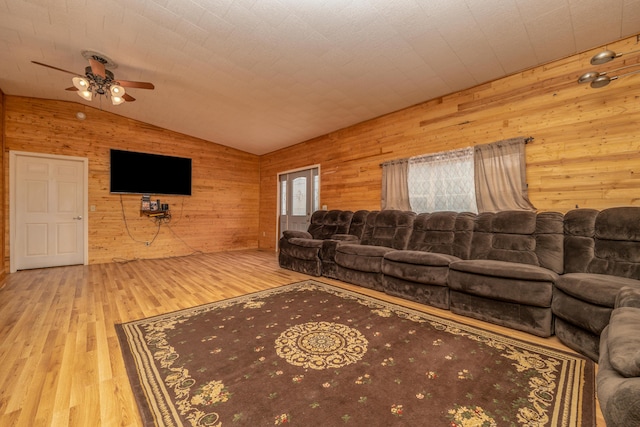 living area featuring lofted ceiling, wooden walls, wood finished floors, and a ceiling fan