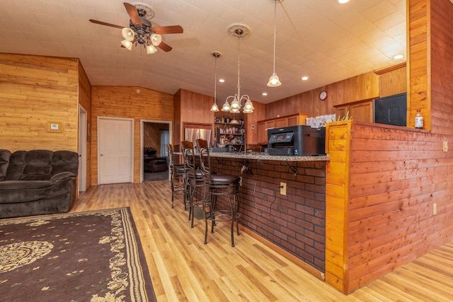 kitchen with brown cabinetry, freestanding refrigerator, vaulted ceiling, light wood-style floors, and wood walls