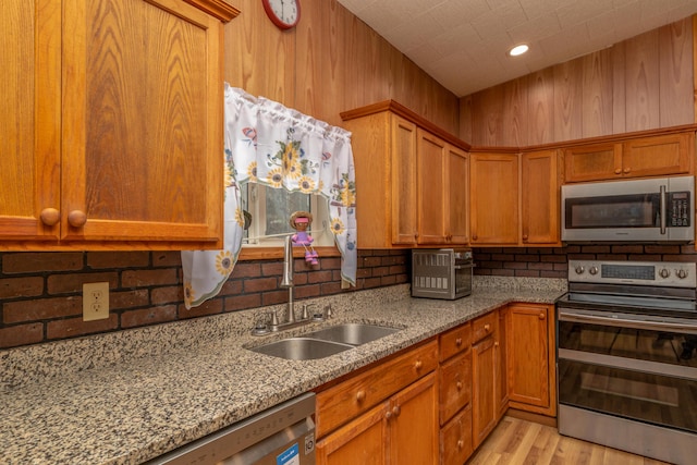 kitchen with light stone counters, brown cabinetry, appliances with stainless steel finishes, and a sink