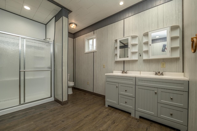 bathroom with toilet, double vanity, a stall shower, wood finished floors, and a sink