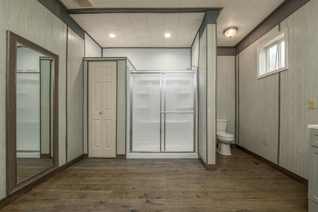 bathroom with toilet, wood finished floors, a stall shower, and wood walls