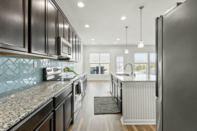 kitchen with a sink, light stone counters, tasteful backsplash, light wood-style floors, and appliances with stainless steel finishes