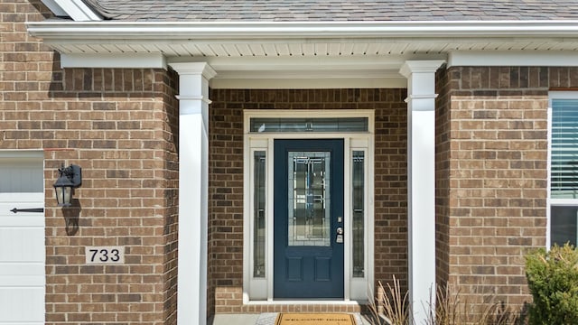 property entrance with a garage, brick siding, and roof with shingles