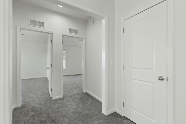 hallway featuring dark colored carpet, visible vents, and baseboards