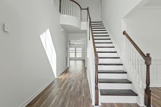 staircase with visible vents, baseboards, a towering ceiling, and wood finished floors