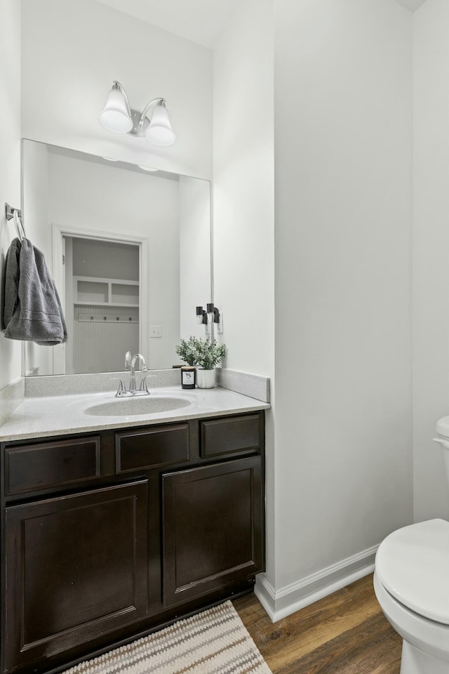 half bathroom featuring baseboards, toilet, wood finished floors, and vanity