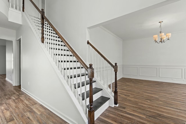 stairway featuring an inviting chandelier, wood finished floors, a towering ceiling, and a decorative wall