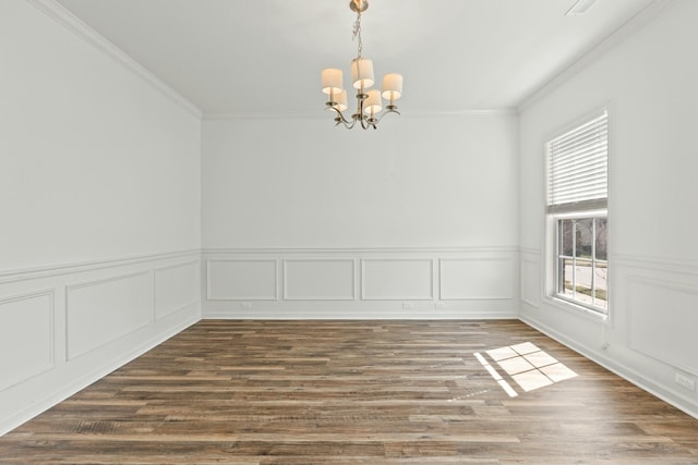 empty room featuring an inviting chandelier, wood finished floors, and ornamental molding