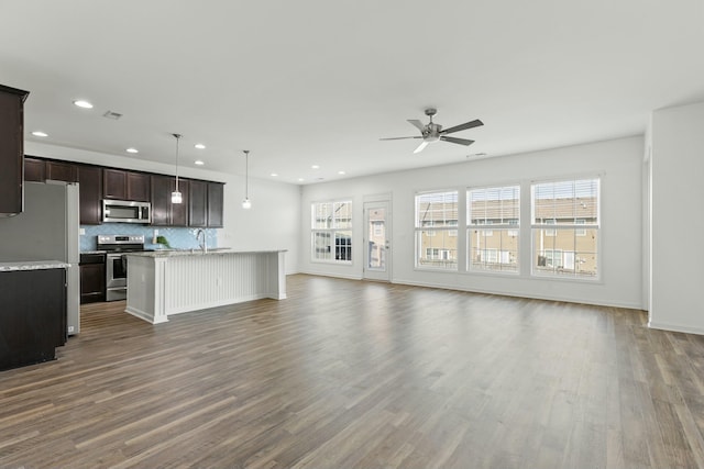 kitchen featuring backsplash, open floor plan, dark wood-style flooring, stainless steel appliances, and a kitchen island with sink