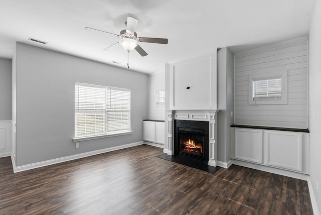 unfurnished living room with visible vents, baseboards, a lit fireplace, a ceiling fan, and dark wood-style flooring