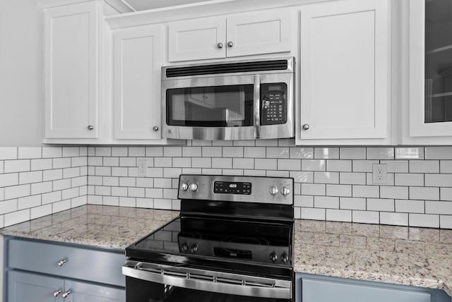 kitchen featuring decorative backsplash, white cabinets, light stone countertops, and stainless steel appliances