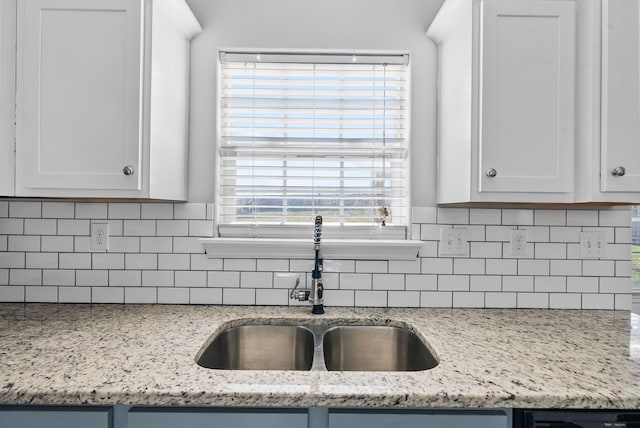 kitchen with white cabinets, light stone countertops, backsplash, and a sink