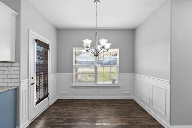 unfurnished dining area featuring an inviting chandelier, dark wood-type flooring, and wainscoting