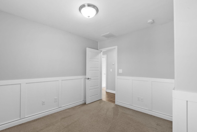 unfurnished room with visible vents, wainscoting, carpet flooring, and a decorative wall