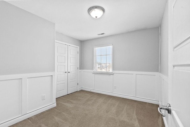 carpeted empty room with visible vents and a wainscoted wall