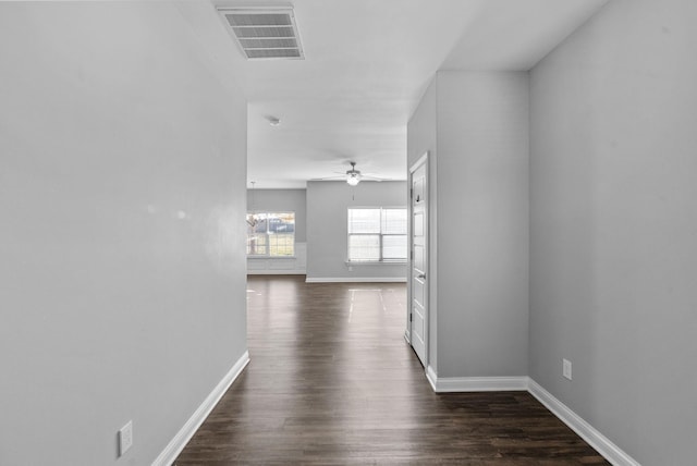 hallway with dark wood-type flooring, baseboards, and visible vents