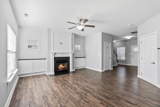 unfurnished living room with a fireplace with flush hearth, a ceiling fan, visible vents, and dark wood-style flooring