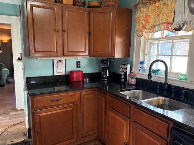 kitchen featuring brown cabinets, dishwasher, dark stone counters, and a sink