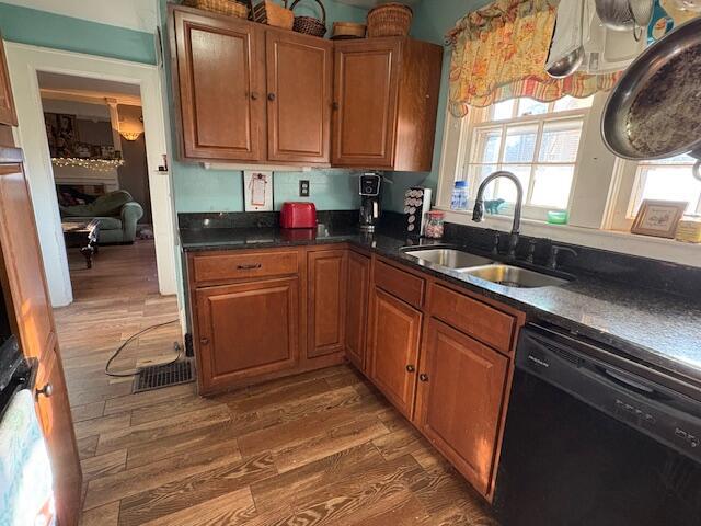 kitchen with wood finished floors, a sink, dishwasher, dark countertops, and brown cabinets