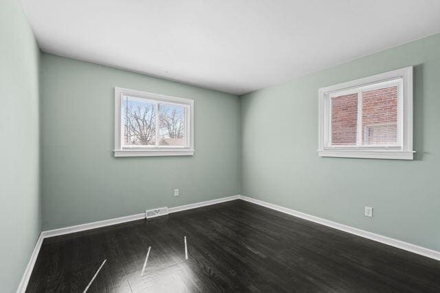 empty room with dark wood finished floors, baseboards, and visible vents