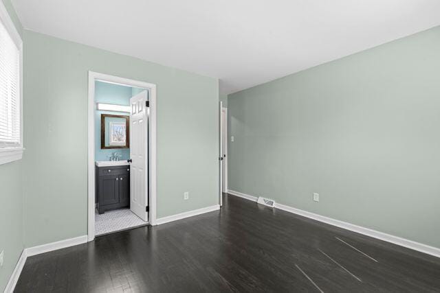 unfurnished bedroom with dark wood finished floors, connected bathroom, baseboards, and a sink