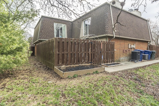 view of home's exterior featuring brick siding, fence, central air condition unit, mansard roof, and a chimney