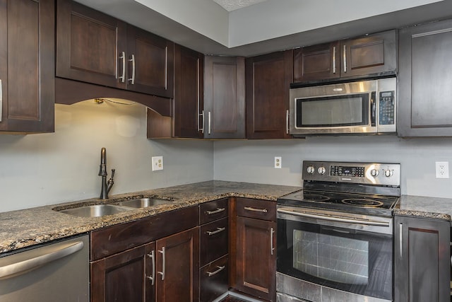 kitchen featuring dark brown cabinetry, appliances with stainless steel finishes, dark stone counters, and a sink