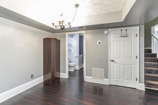 unfurnished bedroom featuring wood finished floors, visible vents, baseboards, ensuite bathroom, and a notable chandelier