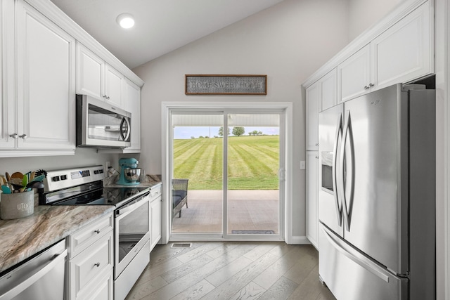 kitchen with light stone countertops, wood finished floors, vaulted ceiling, appliances with stainless steel finishes, and white cabinetry