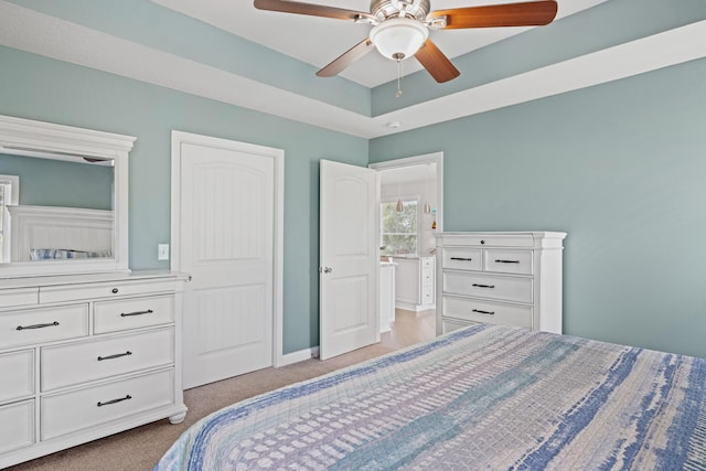 bedroom featuring light carpet, ceiling fan, baseboards, and a tray ceiling