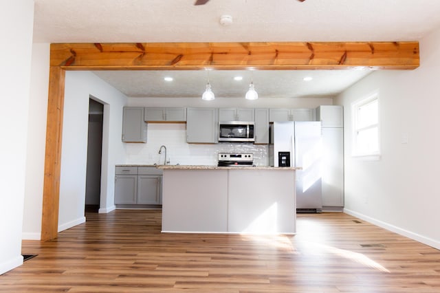 kitchen featuring beam ceiling, gray cabinetry, stainless steel appliances, and light wood-type flooring