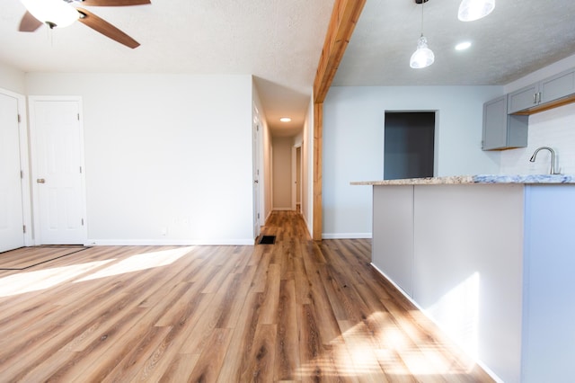 unfurnished living room with baseboards, beamed ceiling, light wood-style flooring, a textured ceiling, and a ceiling fan