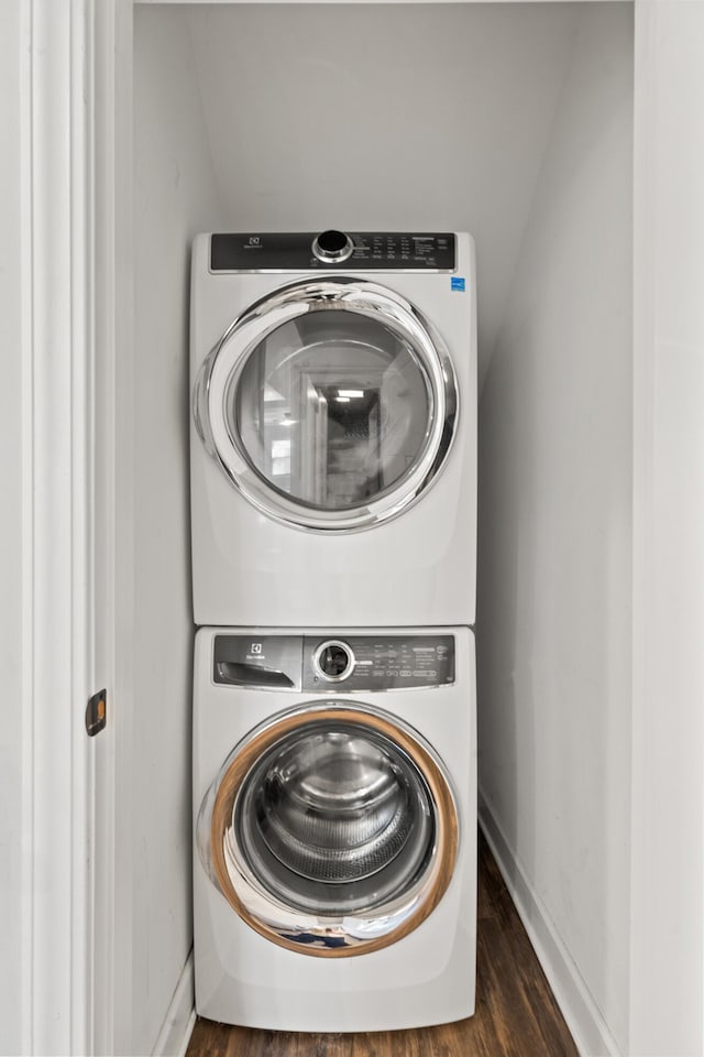 washroom featuring stacked washer and clothes dryer, baseboards, and wood finished floors