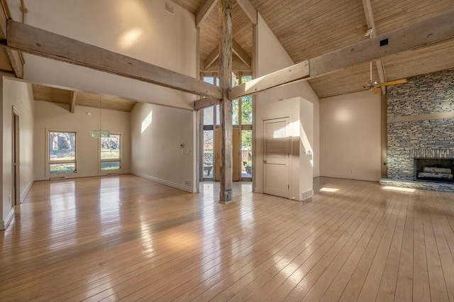 unfurnished living room featuring high vaulted ceiling, beam ceiling, a stone fireplace, a notable chandelier, and light wood-type flooring