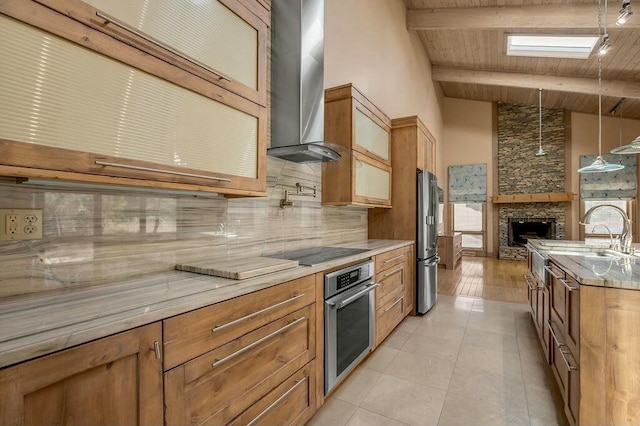 kitchen featuring beam ceiling, a sink, stainless steel appliances, a stone fireplace, and wall chimney range hood