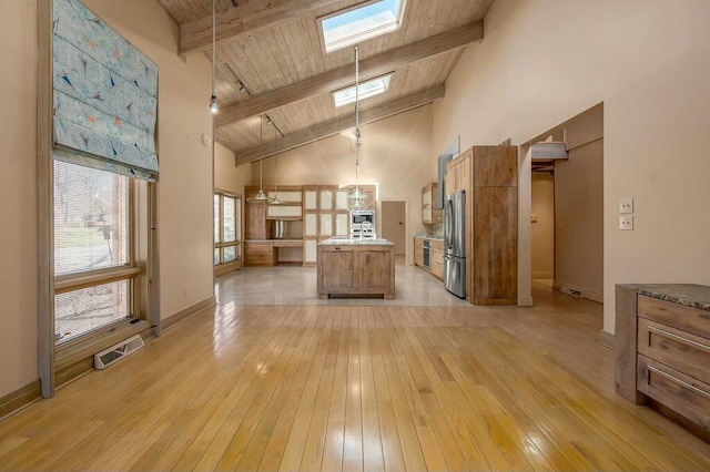 kitchen featuring light wood-type flooring, visible vents, beamed ceiling, freestanding refrigerator, and a skylight