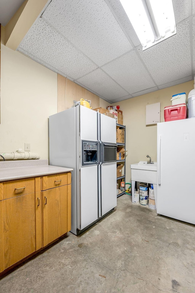 kitchen featuring a drop ceiling, unfinished concrete flooring, white fridge with ice dispenser, and freestanding refrigerator