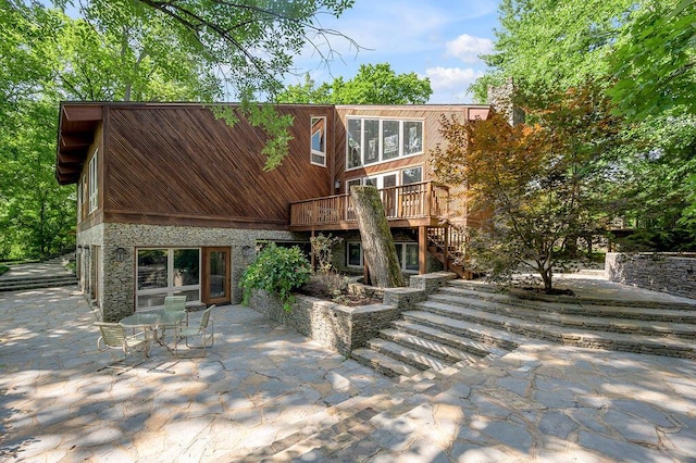 back of house featuring stairway, stone siding, a wooden deck, and a patio area