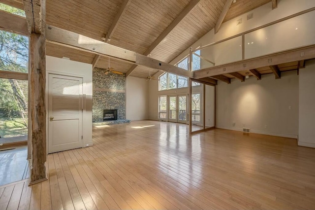 unfurnished living room with high vaulted ceiling, beam ceiling, a fireplace, wood ceiling, and light wood-type flooring