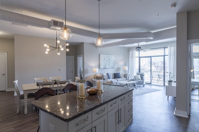 kitchen featuring visible vents, decorative light fixtures, a center island, dark stone counters, and baseboards