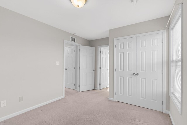 unfurnished bedroom featuring multiple windows, light colored carpet, visible vents, and baseboards