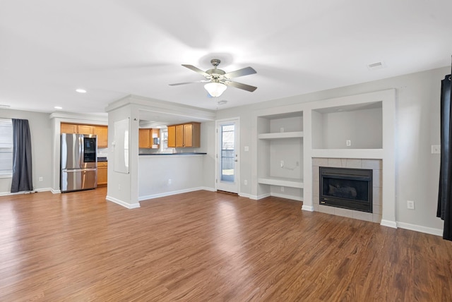 unfurnished living room with a fireplace, built in features, wood finished floors, and baseboards