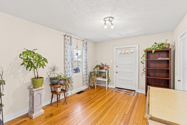 foyer featuring light wood finished floors, a textured ceiling, and baseboards