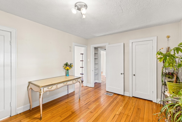bedroom featuring light wood-type flooring, baseboards, visible vents, and a textured ceiling