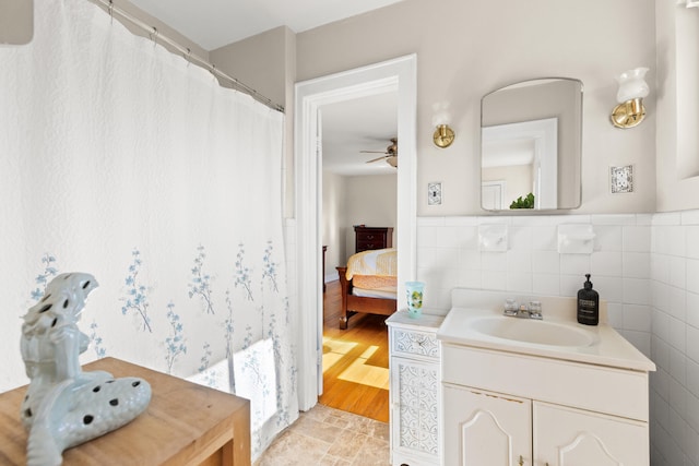 ensuite bathroom with vanity, a ceiling fan, ensuite bathroom, wainscoting, and tile walls