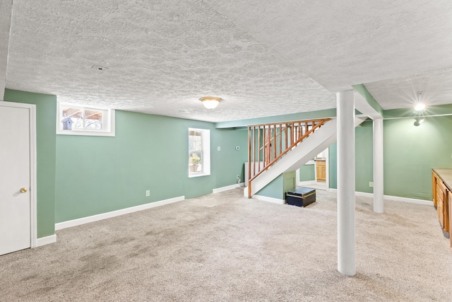 basement with a textured ceiling, a healthy amount of sunlight, carpet flooring, and stairway