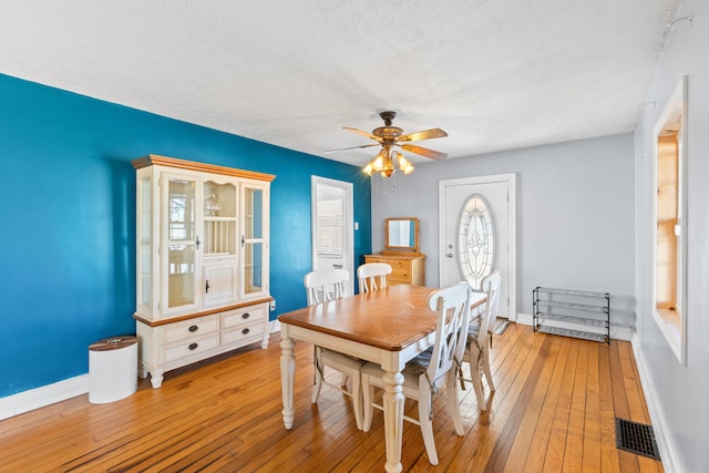dining area featuring hardwood / wood-style floors, baseboards, a ceiling fan, and a textured ceiling