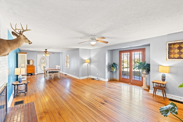 living area featuring a textured ceiling, a ceiling fan, visible vents, light wood finished floors, and baseboards