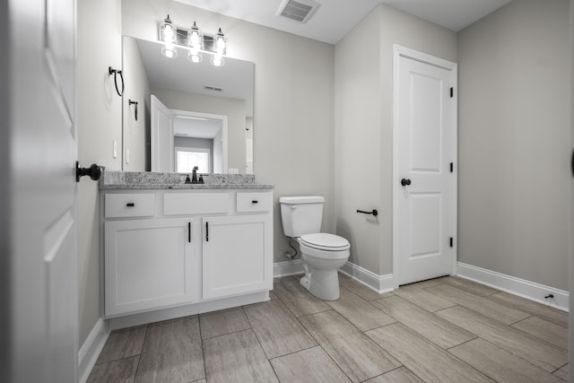 bathroom with vanity, toilet, baseboards, and visible vents