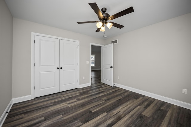 unfurnished bedroom featuring visible vents, baseboards, dark wood-type flooring, and a closet